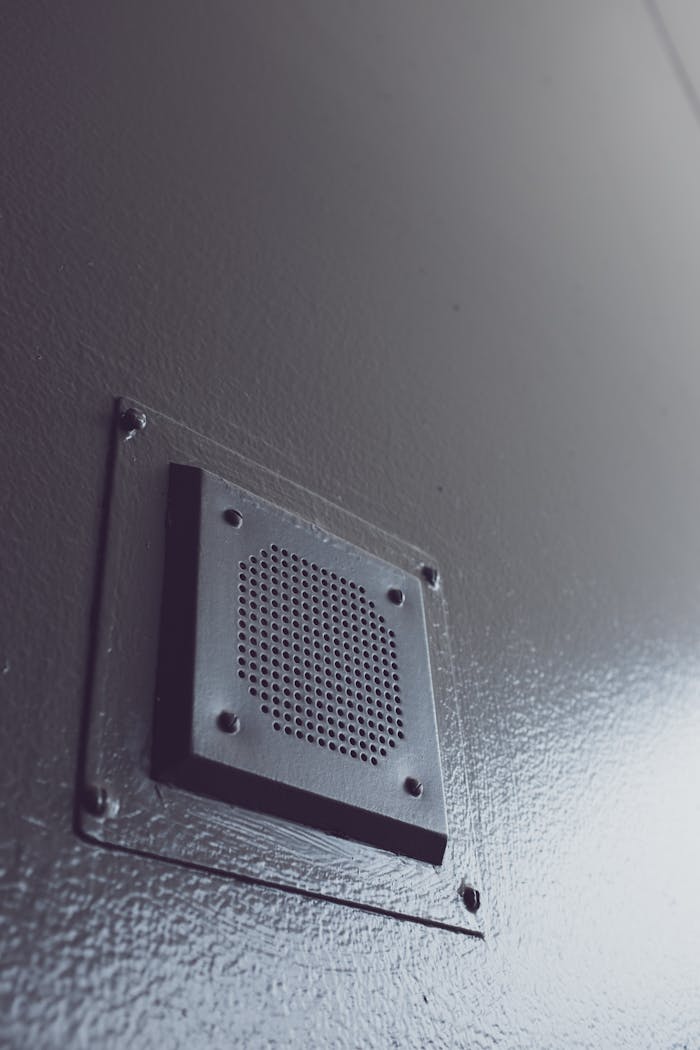 A minimalist close-up shot of a metal ventilation vent on a gray wall.